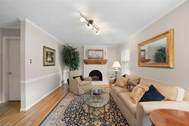 living area featuring ornamental molding, a brick fireplace, baseboards, light wood-type flooring, and a textured ceiling