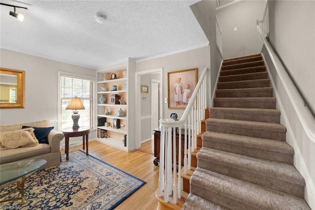 staircase featuring a textured ceiling, ornamental molding, built in shelves, and wood finished floors