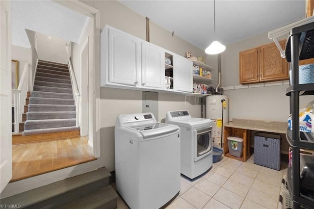 laundry area featuring cabinet space, washing machine and dryer, light tile patterned floors, and water heater