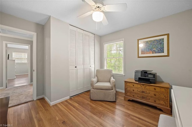 living area featuring light wood-style floors, baseboards, and a ceiling fan
