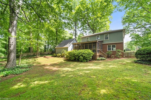 rear view of house featuring fence, a yard, a sunroom, and brick siding