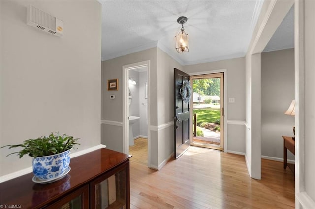 foyer entrance with light wood-style floors, baseboards, crown molding, and a textured ceiling