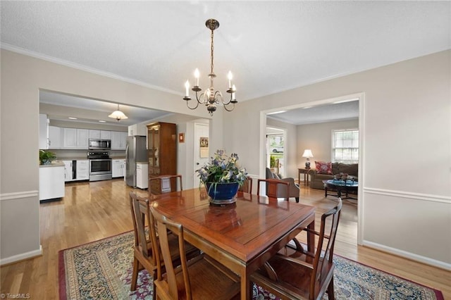 dining space with light wood-type flooring, ornamental molding, baseboards, and a chandelier