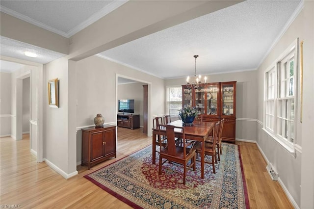dining space with light wood-style floors, a textured ceiling, baseboards, an inviting chandelier, and ornamental molding