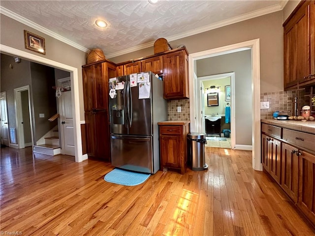 kitchen with backsplash, ornamental molding, light hardwood / wood-style flooring, and stainless steel fridge