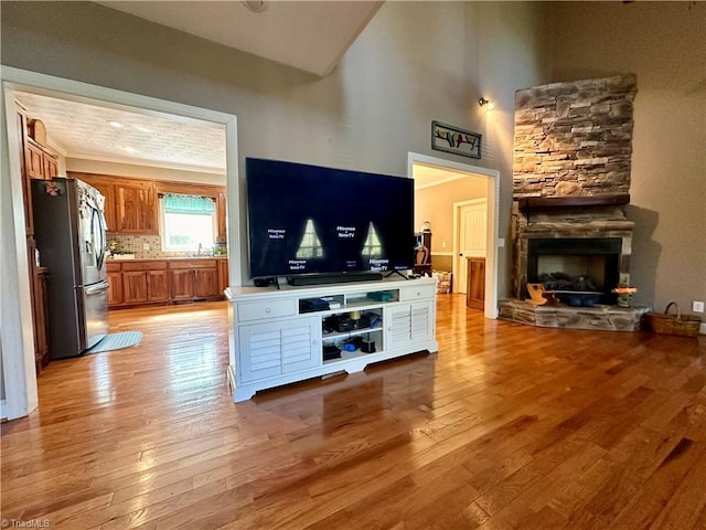 living room with sink, light hardwood / wood-style flooring, a stone fireplace, and a high ceiling