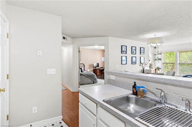 kitchen featuring visible vents, baseboards, light countertops, white cabinetry, and a sink