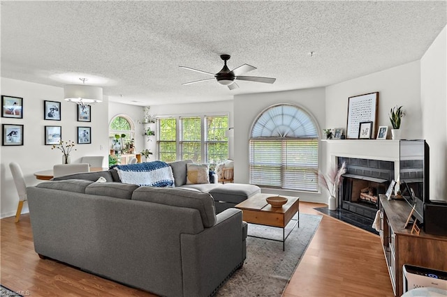 living room featuring a textured ceiling, ceiling fan, wood finished floors, and a tile fireplace