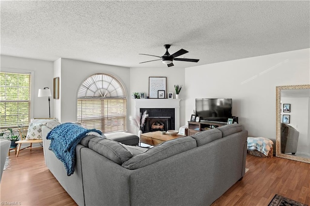 living room featuring a textured ceiling, ceiling fan, wood finished floors, and a tile fireplace