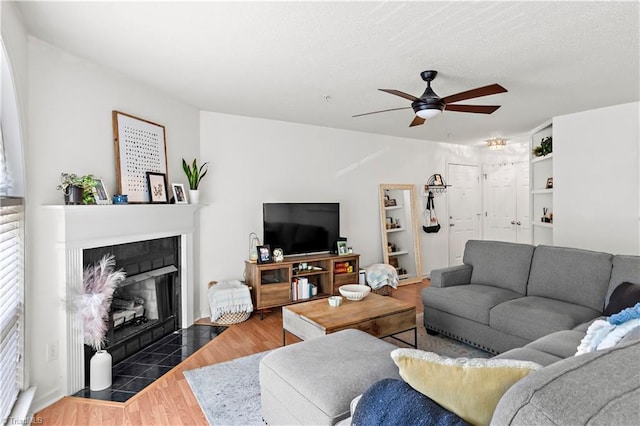 living room featuring a tiled fireplace, a ceiling fan, and wood finished floors