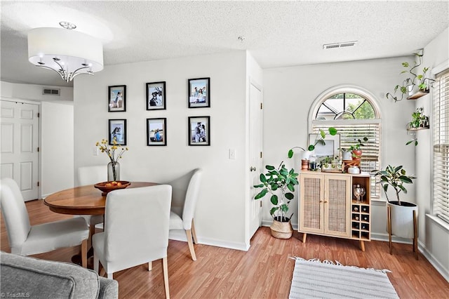 dining area with visible vents, a textured ceiling, light wood-style flooring, and baseboards