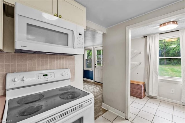 kitchen featuring baseboards, backsplash, light tile patterned flooring, and white appliances