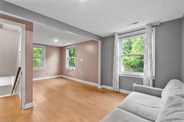 unfurnished living room with a textured ceiling, visible vents, baseboards, and light wood-style flooring