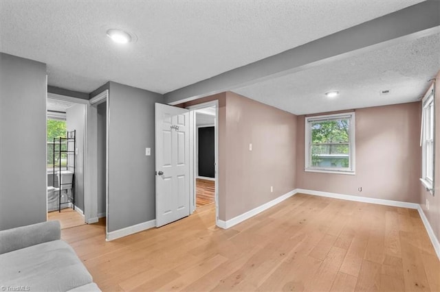 unfurnished living room featuring a textured ceiling, a wealth of natural light, baseboards, and light wood-style flooring