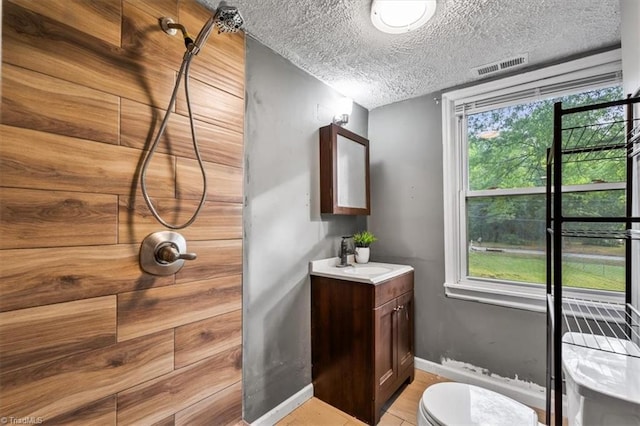 bathroom featuring visible vents, vanity, toilet, baseboards, and tiled shower