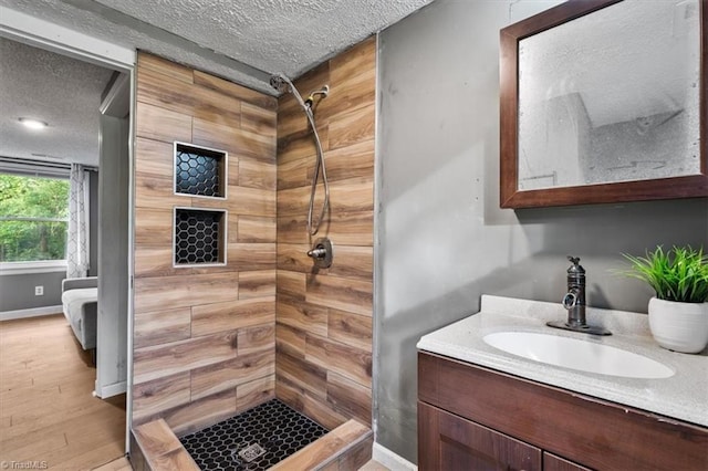 full bathroom featuring vanity, wood finished floors, baseboards, a textured ceiling, and a shower stall