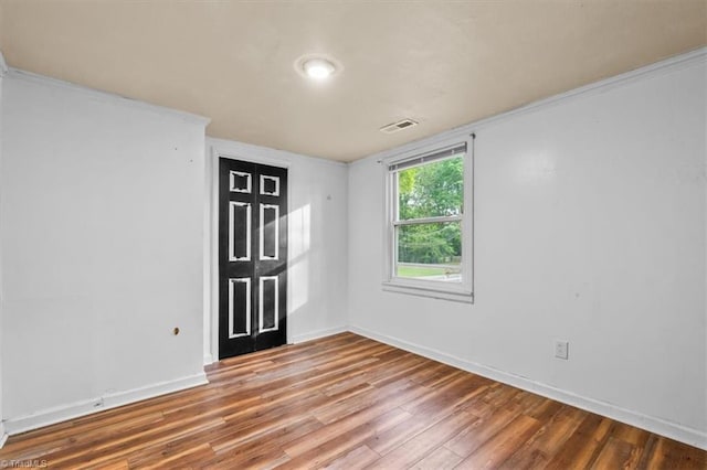 spare room featuring visible vents, ornamental molding, baseboards, and wood finished floors