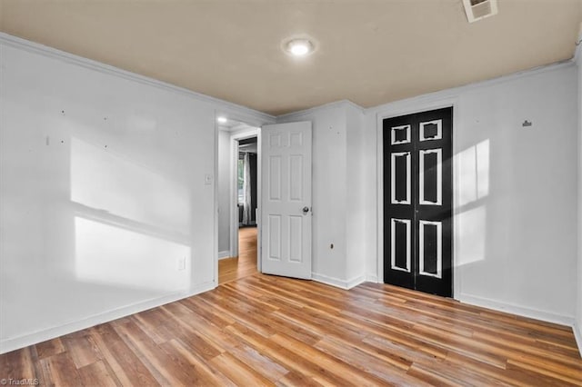 empty room with baseboards, ornamental molding, light wood finished floors, and visible vents