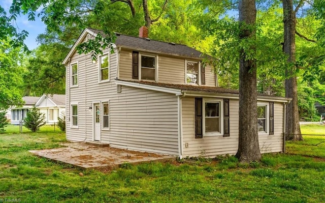 rear view of house featuring a yard, fence, a chimney, and a patio area