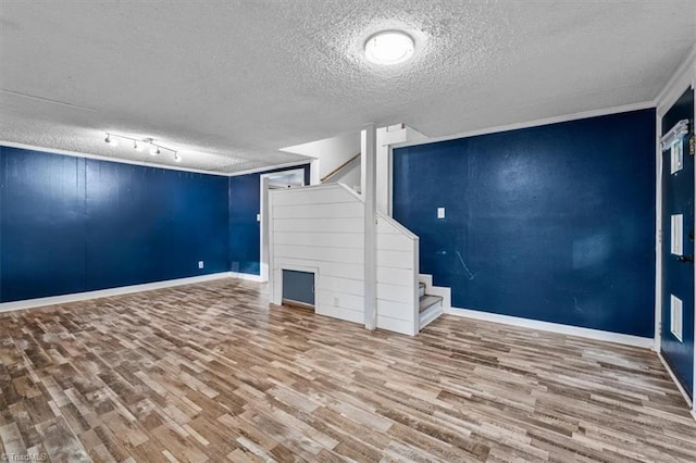 finished below grade area with stairs, a textured ceiling, baseboards, and wood finished floors