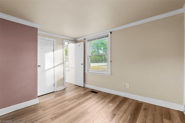 empty room featuring baseboards, light wood-style flooring, crown molding, and visible vents