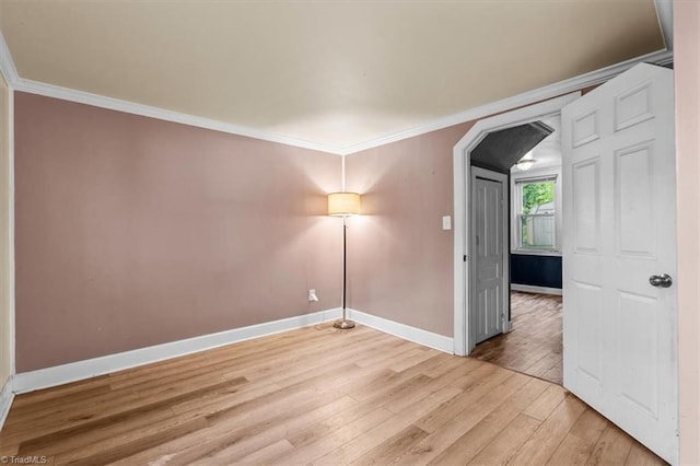 empty room with baseboards, arched walkways, light wood finished floors, and crown molding