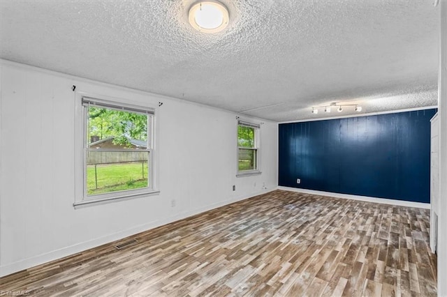 unfurnished room with a textured ceiling, plenty of natural light, and wood finished floors