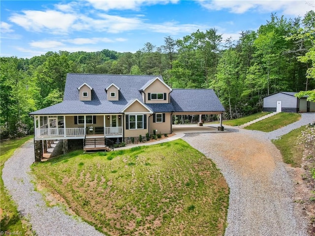 view of front of house with a porch, driveway, a view of trees, and a front yard