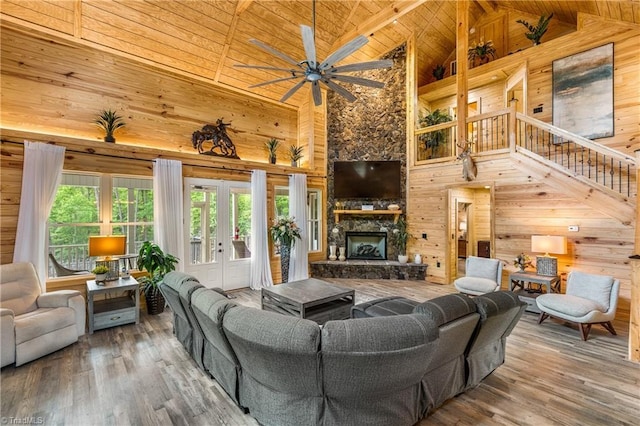 living area with wooden walls, wooden ceiling, high vaulted ceiling, a ceiling fan, and wood finished floors
