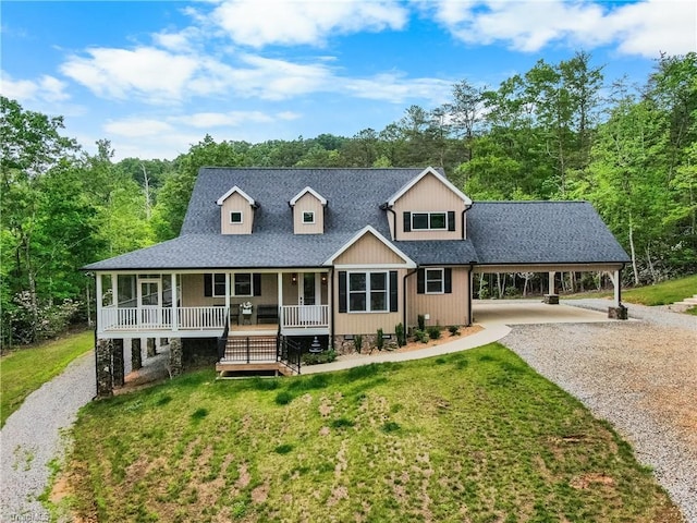 view of front of house with gravel driveway, covered porch, a front yard, roof with shingles, and a wooded view