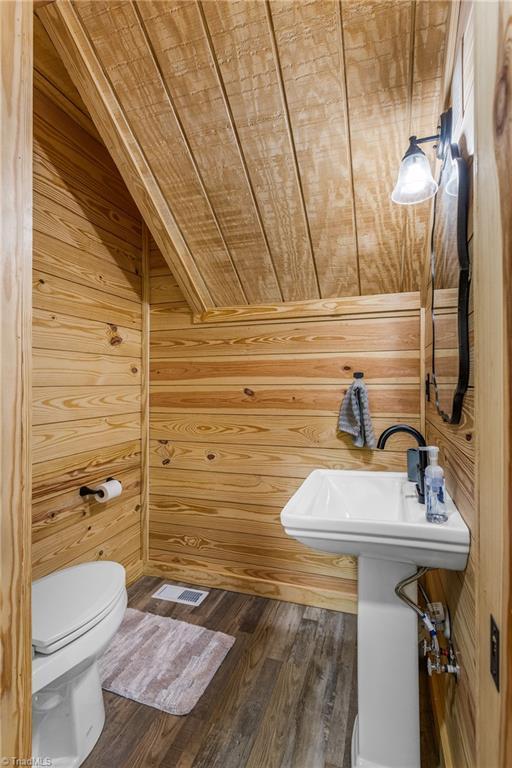 half bathroom with wooden walls, toilet, wood finished floors, and wood ceiling