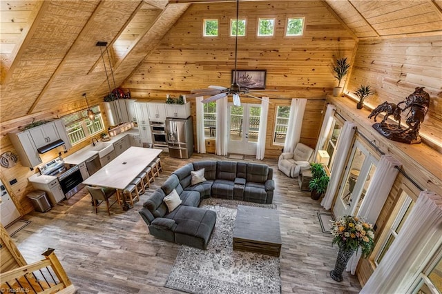 living room featuring wooden walls, high vaulted ceiling, wooden ceiling, wood finished floors, and healthy amount of natural light