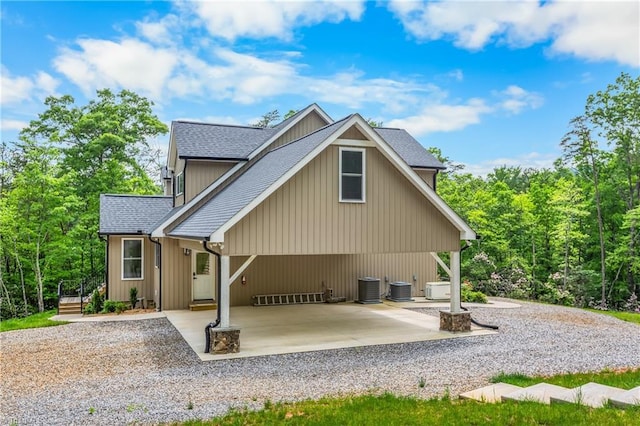 rear view of property with driveway, central AC, and a shingled roof