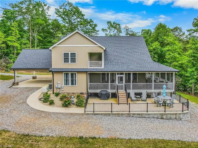 view of front facade featuring a shingled roof, a sunroom, gravel driveway, and a patio area