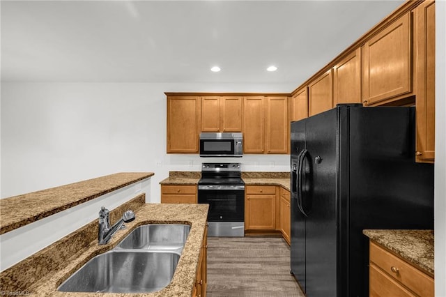 kitchen with brown cabinets, a sink, stone countertops, recessed lighting, and appliances with stainless steel finishes