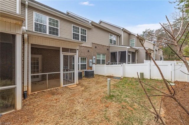 rear view of house with fence, brick siding, and a sunroom