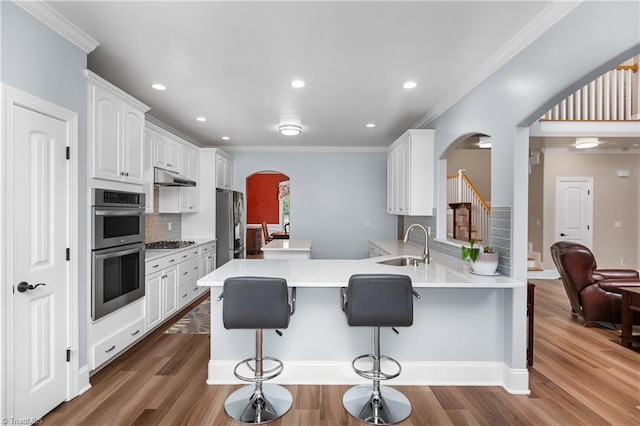 6147 Olde Fields Way, Pfafftown, NC 27040 - kitchen with arched walkways, stainless steel appliances, under cabinet range hood, a breakfast bar area, and decorative backsplash