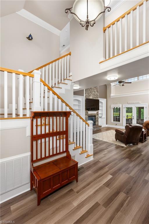 6147 Olde Fields Way, Pfafftown, NC 27040 - staircase with a towering ceiling, wood finished floors, a stone fireplace, a ceiling fan, and crown molding