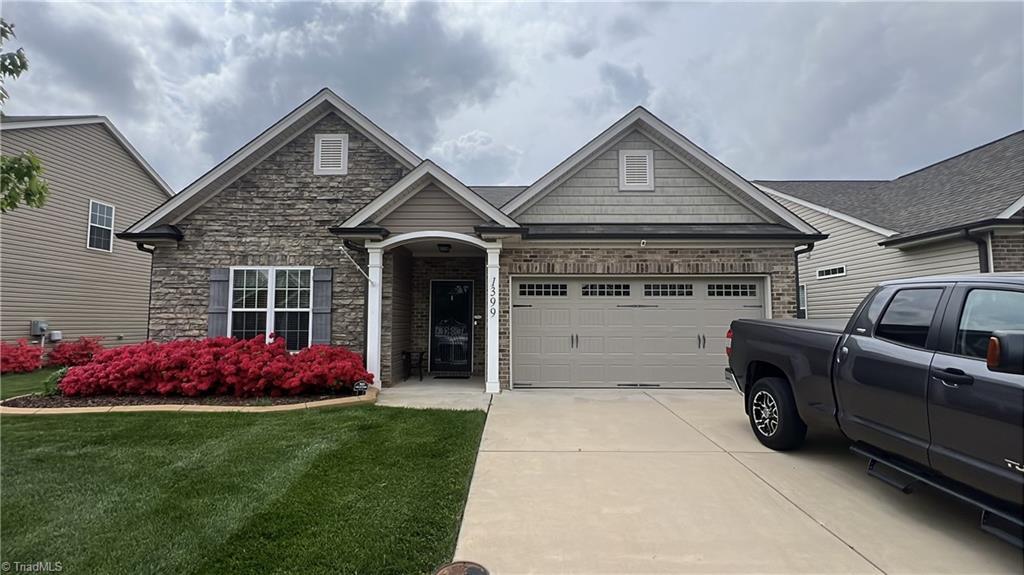 craftsman inspired home featuring a front yard, driveway, stone siding, and an attached garage