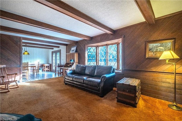 carpeted living room with wooden walls, a textured ceiling, and beam ceiling