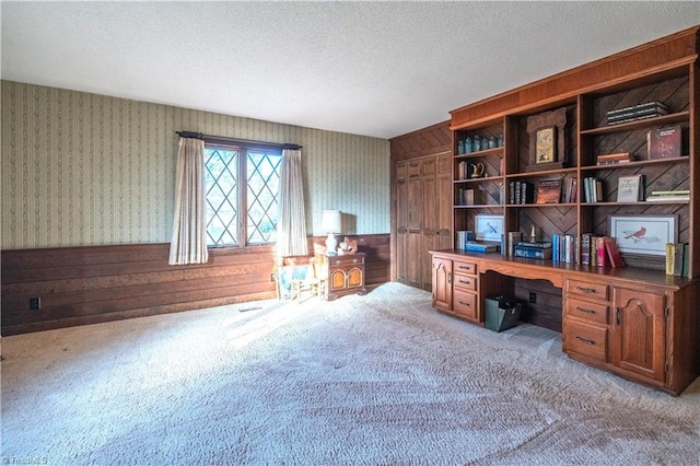 carpeted office space with wood walls, built in desk, and a textured ceiling