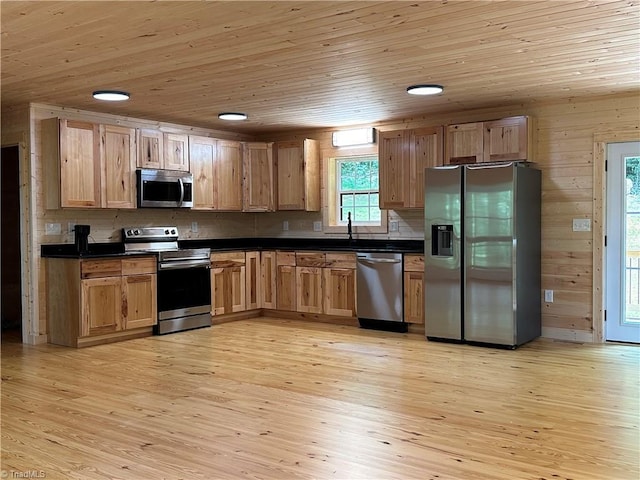 kitchen with wooden ceiling, stainless steel appliances, wooden walls, and light hardwood / wood-style flooring