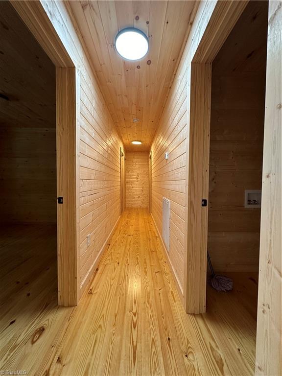 corridor with wooden walls, light hardwood / wood-style flooring, and wooden ceiling