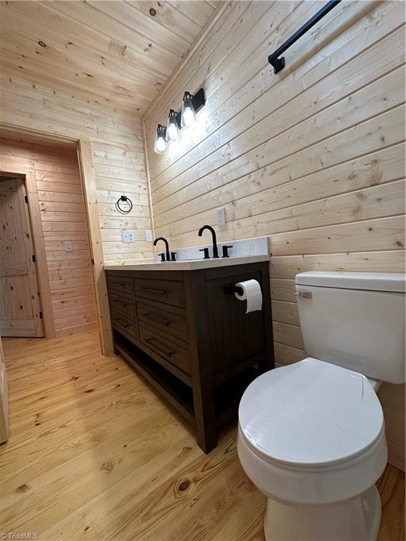 bathroom featuring hardwood / wood-style floors, vanity, wood walls, and wood ceiling