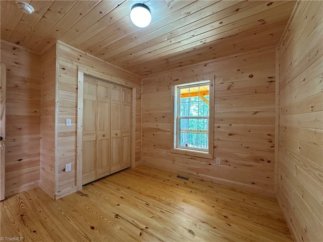 unfurnished bedroom featuring wood walls, light hardwood / wood-style floors, wooden ceiling, and a closet