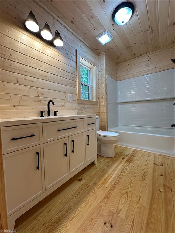 full bathroom with hardwood / wood-style floors, vanity, wooden ceiling, wooden walls, and toilet