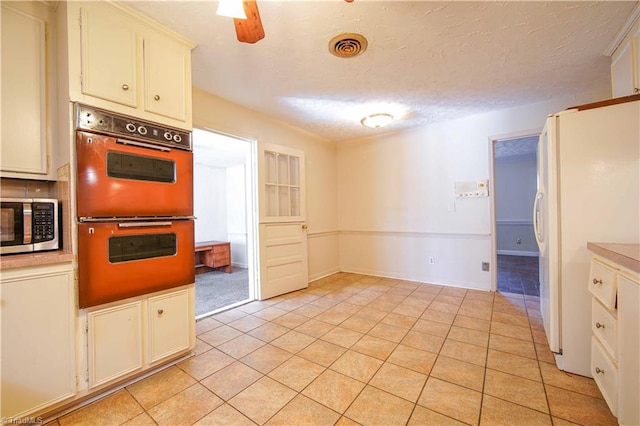 kitchen with white refrigerator, light tile patterned floors, a textured ceiling, double oven, and white cabinetry