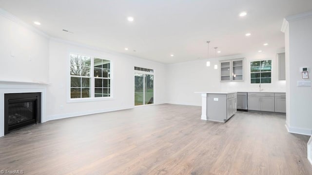 unfurnished living room with light wood-type flooring, ornamental molding, a glass covered fireplace, recessed lighting, and baseboards