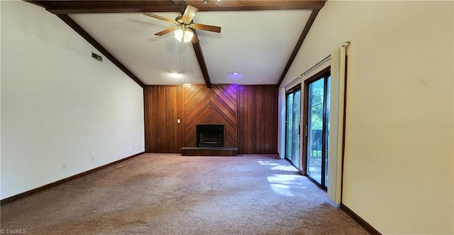 unfurnished living room with wooden walls, ceiling fan, a fireplace, vaulted ceiling with beams, and carpet