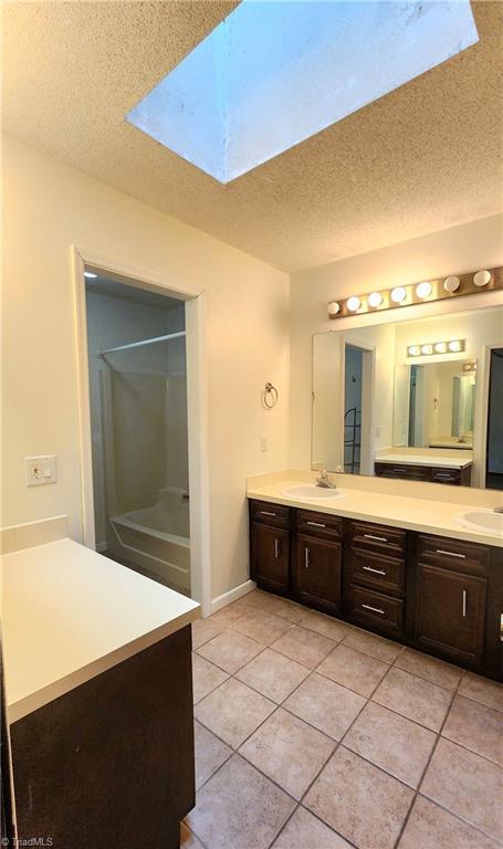 bathroom with double vanity, a skylight, a sink, a textured ceiling, and tile patterned floors